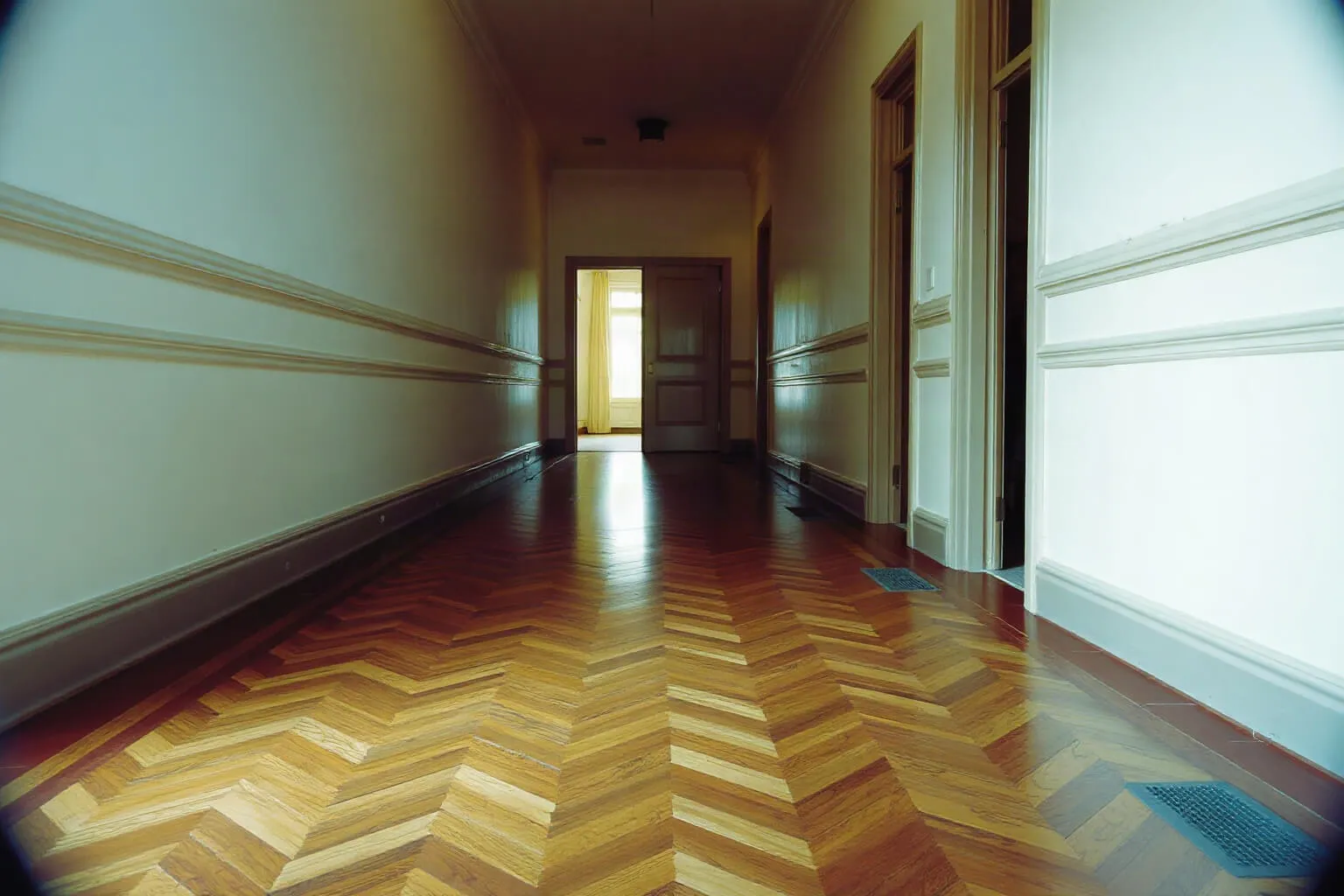 Lungo disimpegno con pavimento in noce a chevron e porte a pannelli
