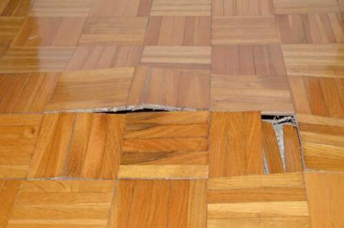 Immagine di un parquet gonfiato a causa di una infiltrazione d'acqua, un problema comune con i pavimenti in legno bagnati.